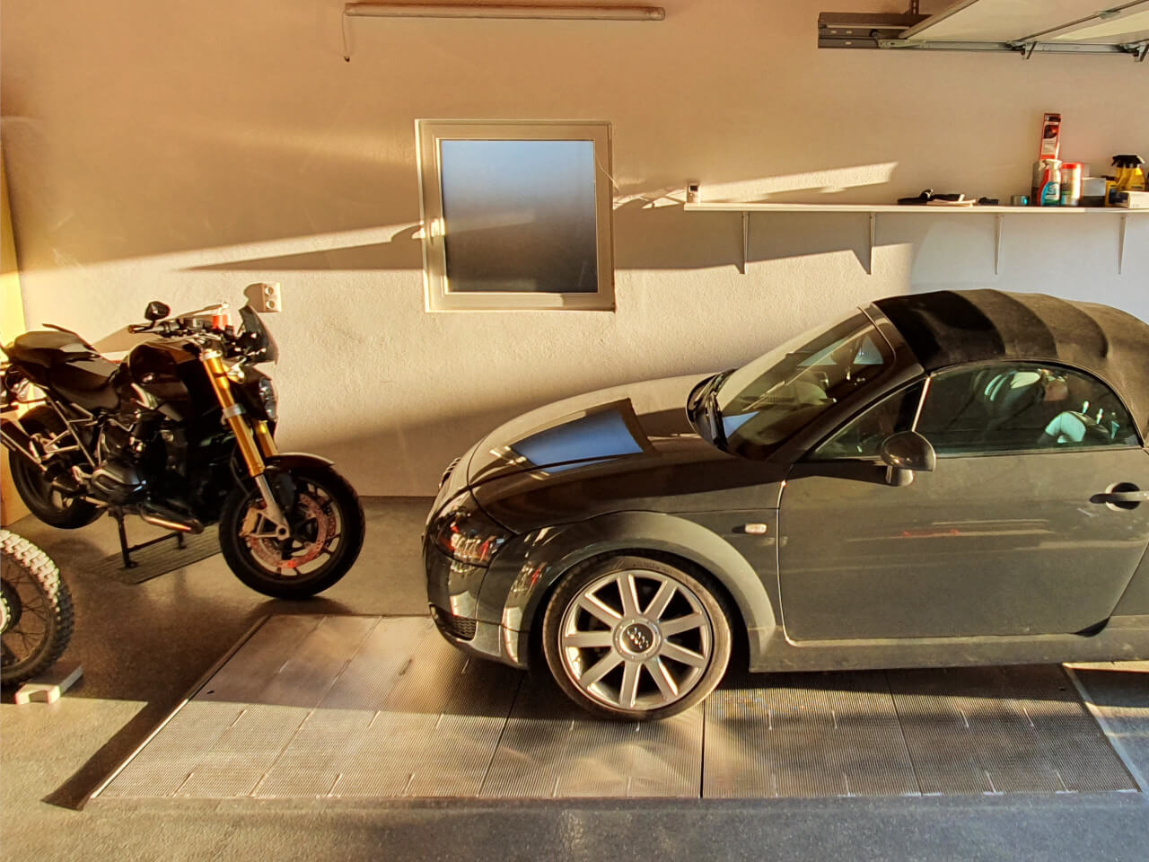 pkw und motorrad stehen auf einer grube mit abdeckung in einer garage