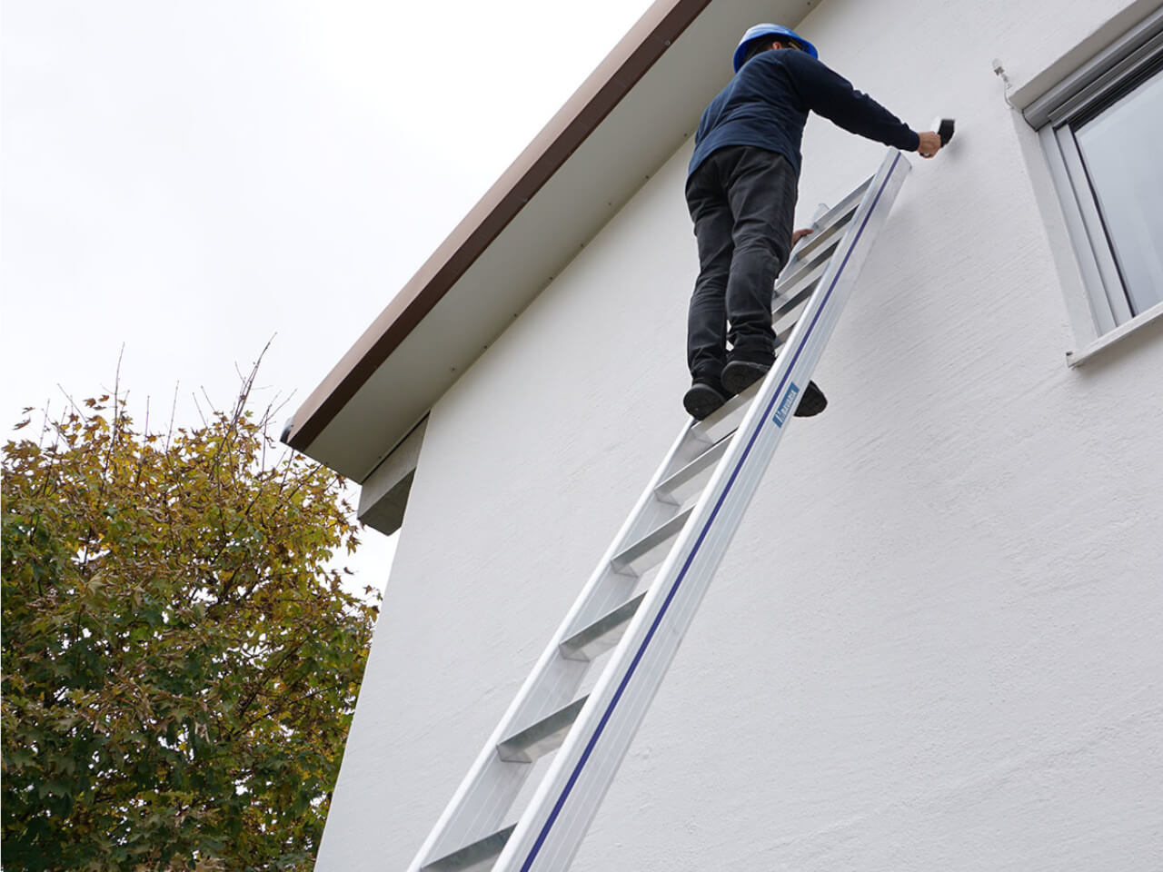 person steht auf alu anlegeleiter anlehnend an hauswand