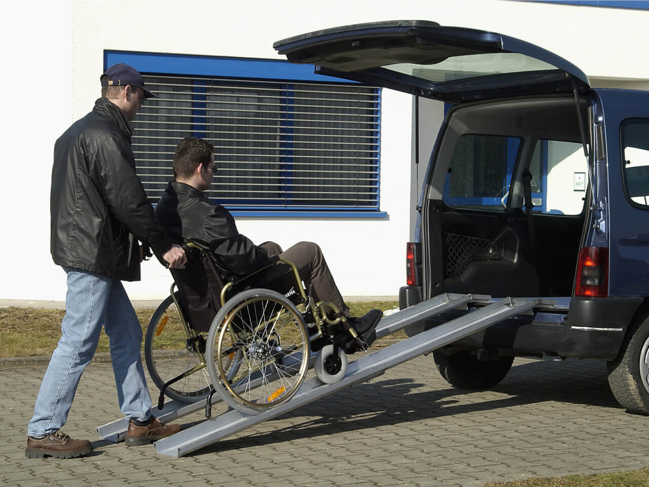 rollstuhlfahrer wird mithilfe einer klappbaren rollstuhlrampe ins auto gefahren