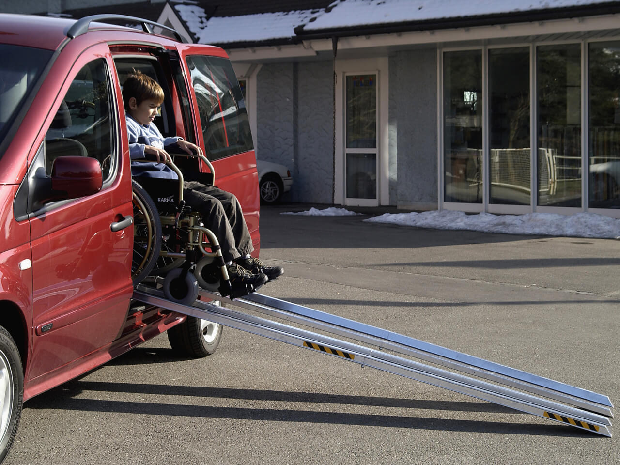 kind im rollstuhl faehrt ueber rollstuhlrampe aus auto