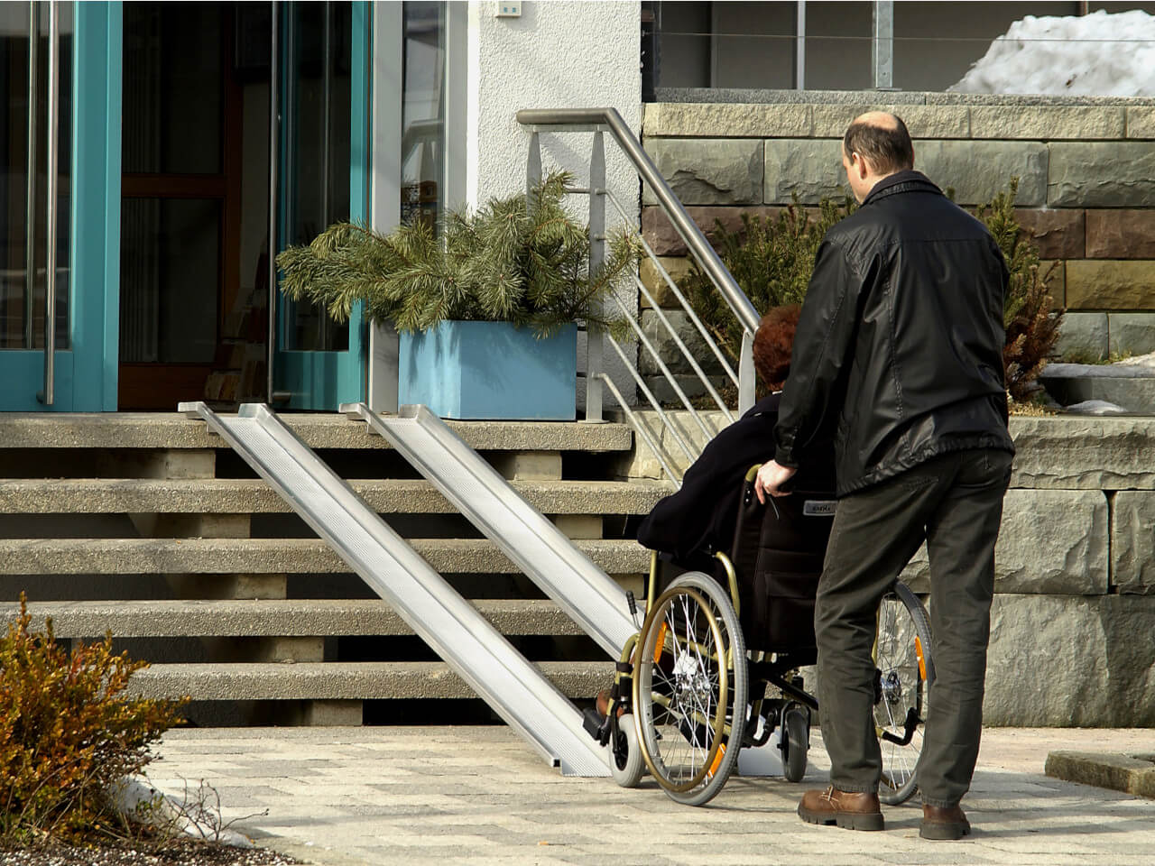 rollstuhlfahrer wird mithilfe von rollstuhlrampen ueber eine treppe geschoben