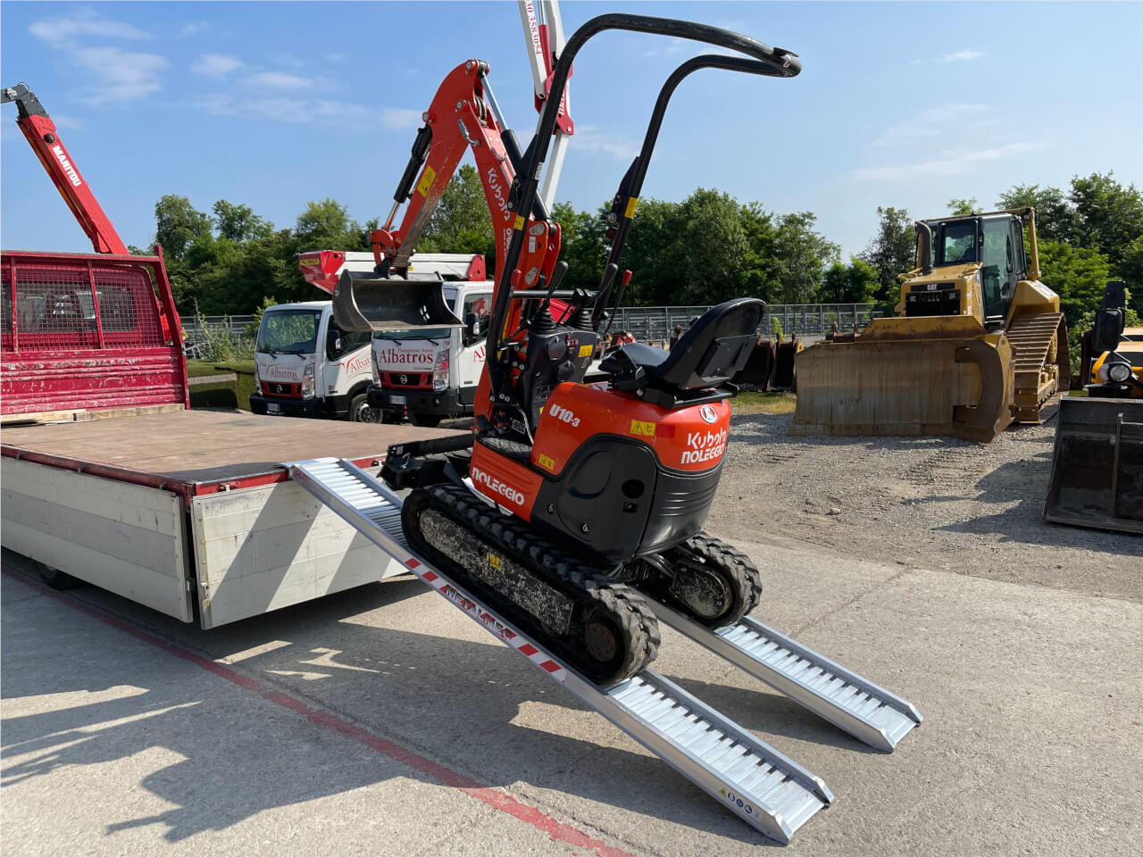 kleiner bagger mit gummiketten fahert ueber auffahrrampen auf transportfahrzeug