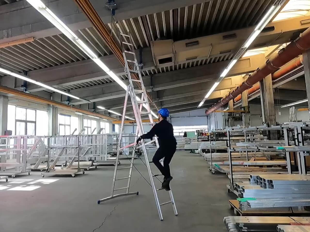 mann steigt auf alu mehrzweckleiter in einer halle fuer deckenarbeiten