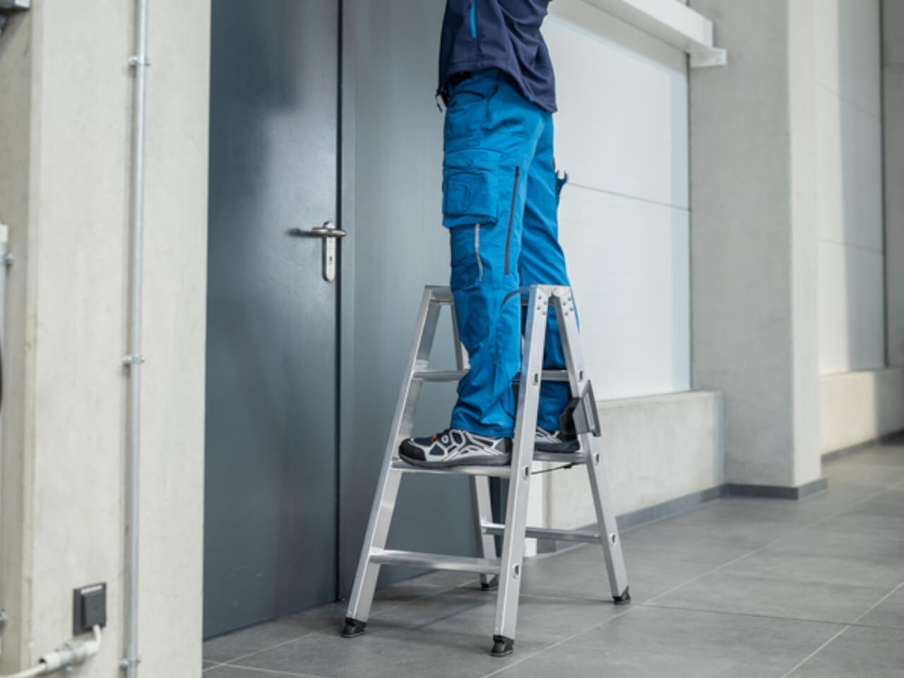 mechaniker am aufzug steht auf einer beidseitig begehbaren stufen-stehleiter von munk