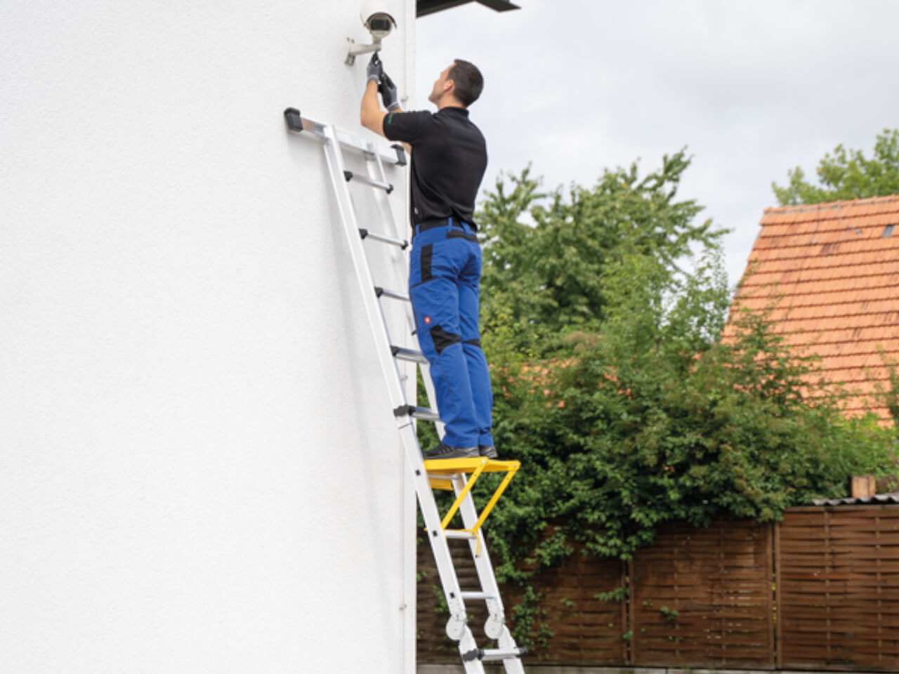 wandmontage einer kamera durch einen handwerker stehend auf einer munk teleskopleiter mit traverse