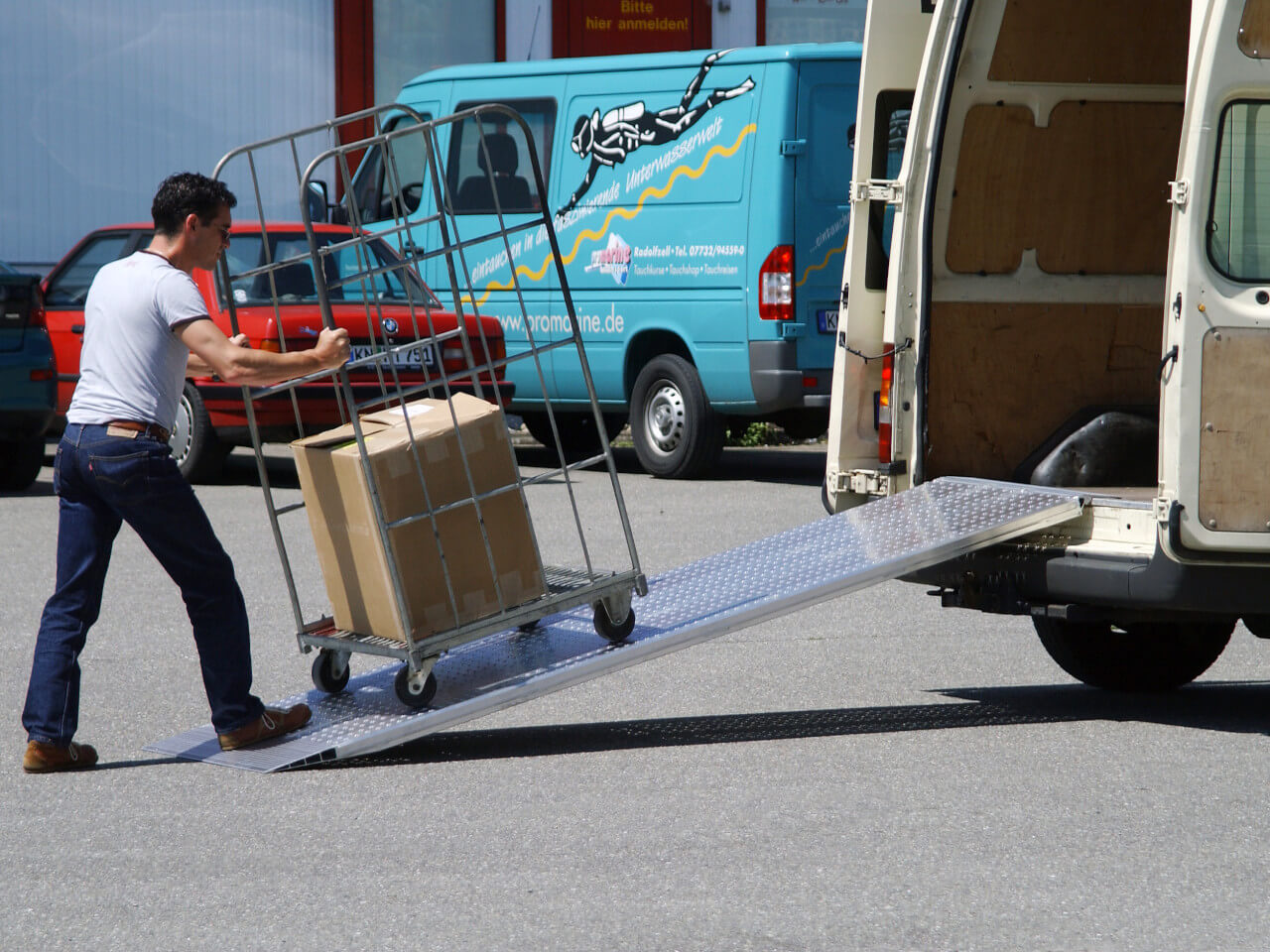 mann faehrt mit transportwagen ueber eine auffahrrampe in einen transporter