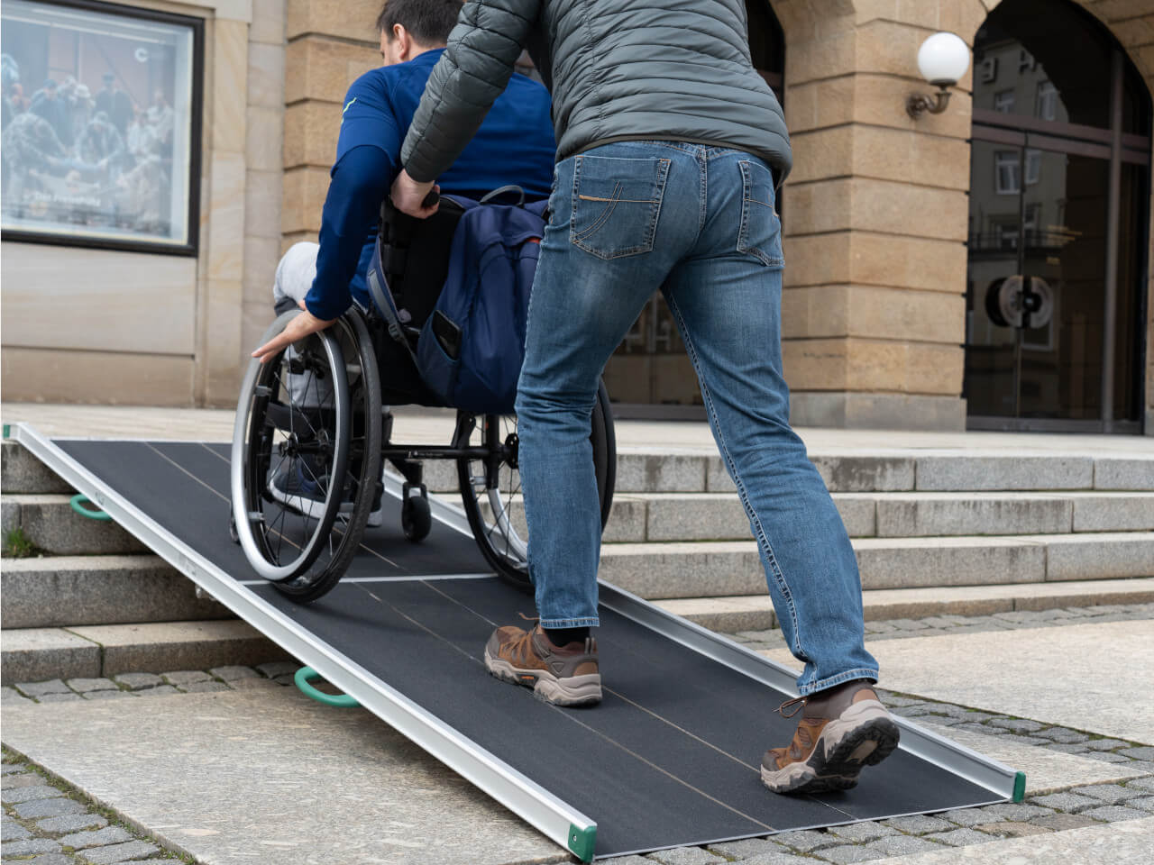 rollstuhlrampe an treppe wird von rollstuhlfahrer mit hilfsperson benutzt