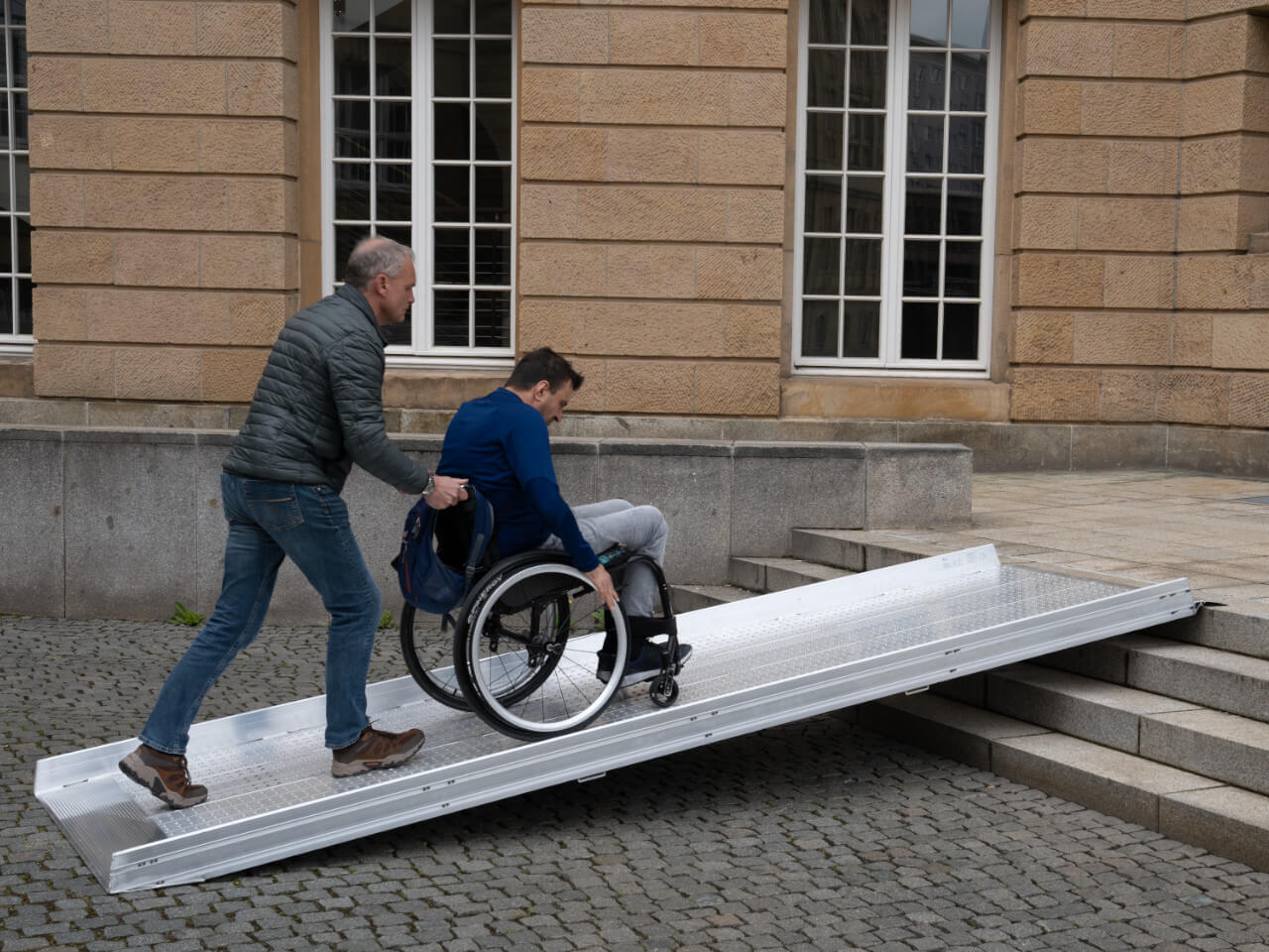 rollstuhlfahrer mit hilfsperson nutzt aol-r rollstuhlrampe fuer 4 stufen an einer treppe